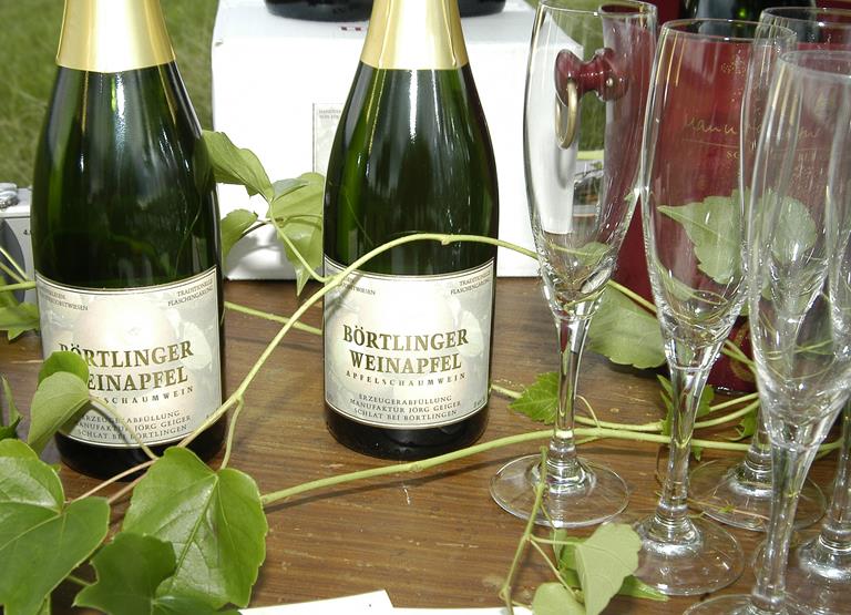 Auf diesem Bild sind zwei Flaschen des Schaumweins "Börtlinger Weinapfel" abgebildet sowie einige Sektgläser.