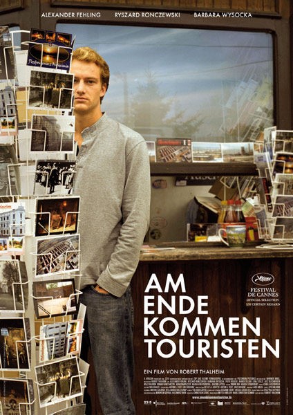 Auf dem Bild sieht man einen Mann in Jeans und einem hellen Pullover, der Vor einem Postkartenständer steht. Hinter ihm auf einem Regal stehen ebenfalls Postkartenständer.