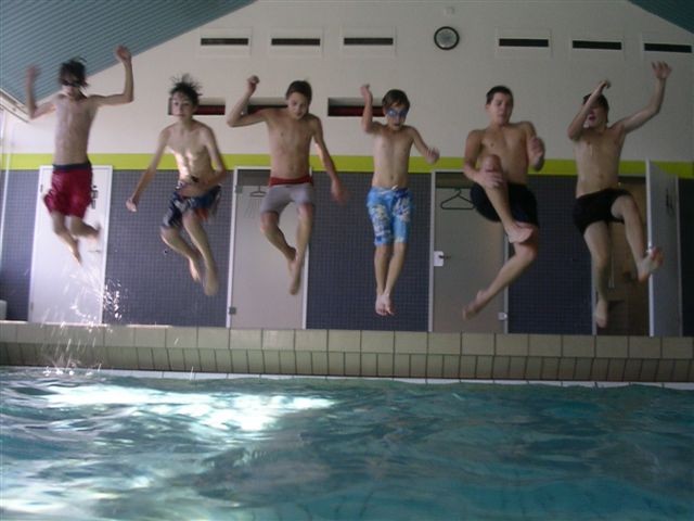 Auf dem Bild hüpfen sechs Jungs nebeneinander in ein Schwimmbecken.
