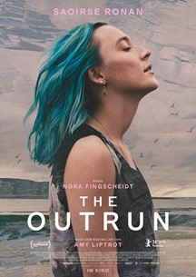 Auf dem Bild sieht man eine junge Frau mit blauen Haaren. Sie trägt ein ärmelloses schwarzes T-Shirt. Im Hintergrund sieht man den Himmel und das Meer.