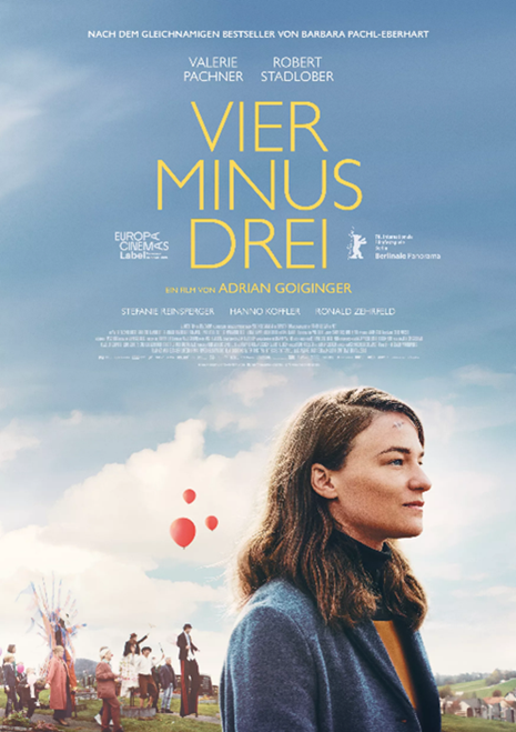 Auf dem Plakat sieht man im Vordergrund eine Frau von der Seite. Sie hat lange braune Haare und trägt einen blauen Mantel. Im Hintergrund sieht man mehrere Menschen, die rote Luftballons steigen lassen.